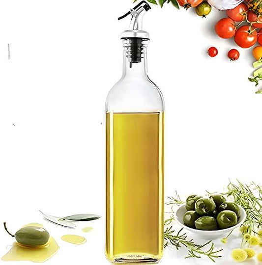 Clear glass oil dispenser bottle for kitchen with a pouring spout and fresh ingredients around