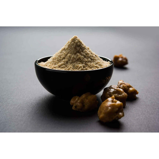 Black bowl filled with organic asafoetida powder surrounded by asafoetida pieces for cooking flavor enhancement