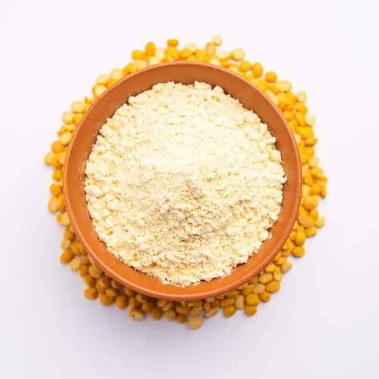 Brown bowl filled with organic besan flour, surrounded by yellow split peas, perfect for cooking and baking