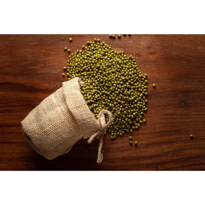 Brown burlap sack spilling organic green moong beans on a wooden surface, perfect for cooking and healthy eating
