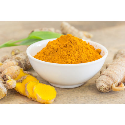 Organic haldi powder in a white bowl with fresh turmeric roots on a wooden surface
