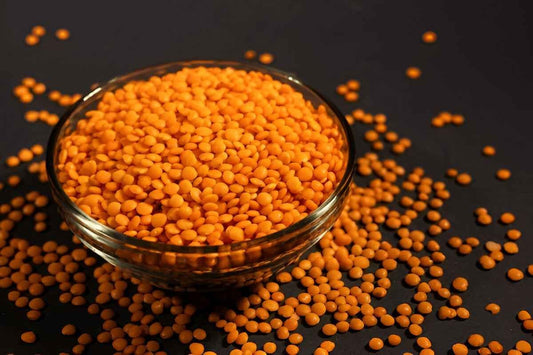 Bowl of orange organic masoor dal scattered on a dark surface, perfect for healthy soups and dishes