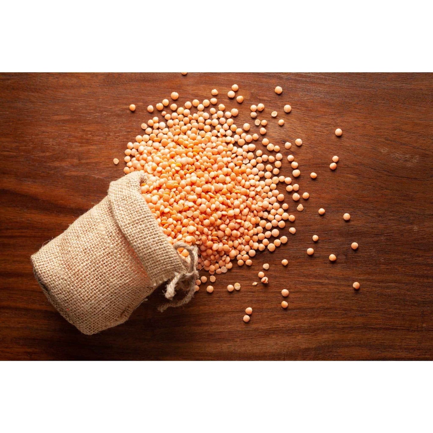 Organic masoor dal in a burlap sack with loose lentils scattered on a wooden surface