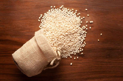 White Organic Urad Dal spilled from a burlap sack on a wooden surface, ideal for cooking nutritious meals