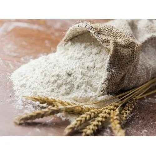 Organic wheat flour in a burlap sack spilled on a wooden surface with golden wheat stalks