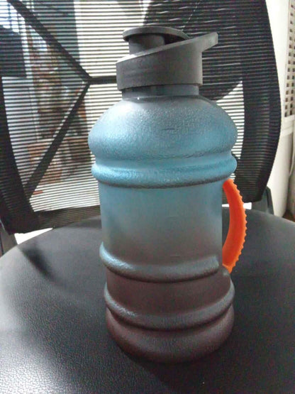 Reusable fitness water jug by THE GIR FARMER with black lid and orange handle on black chair