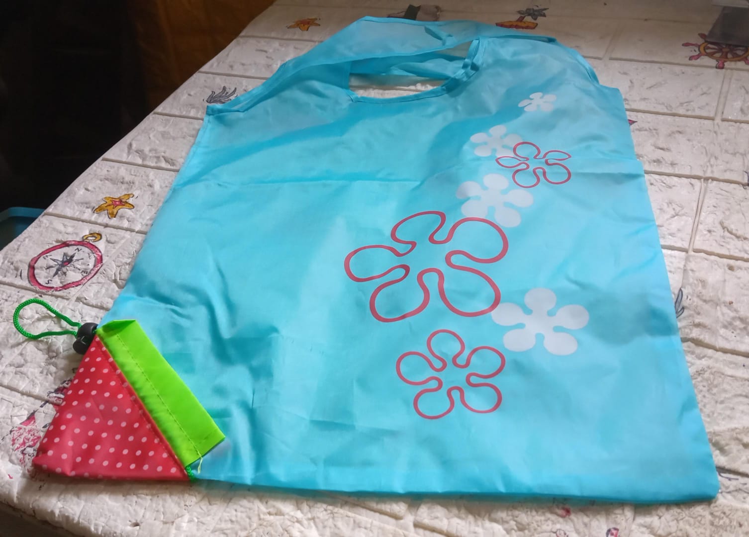 Light blue reusable grocery bag with handles featuring colorful flower designs, folds for easy storage