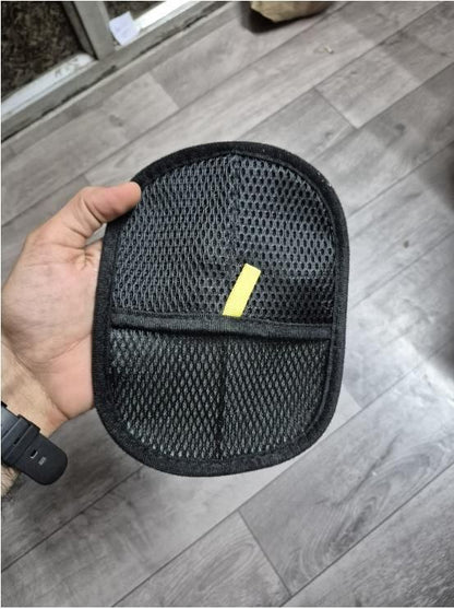 Black mesh pet hair removal gloves mitt with yellow pull tab held in hand over gray wood floor