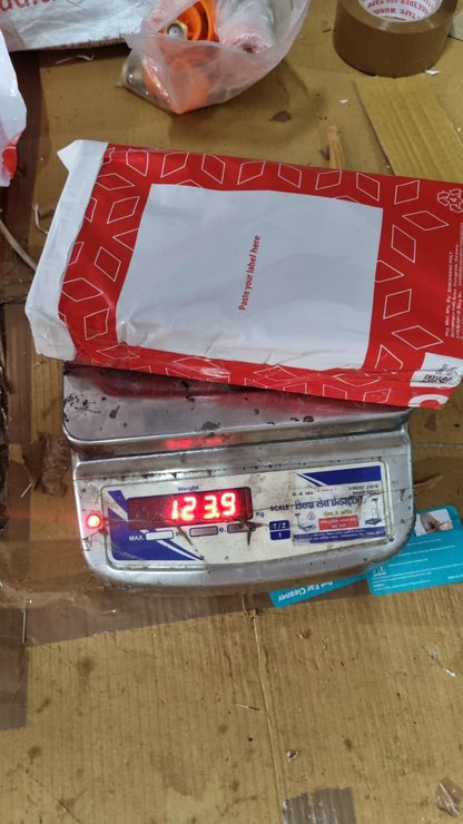 Red and white shipping package with pet hair removal gloves on digital scale reading about 124 grams on a cardboard workbench