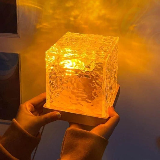 A hands holding a glowing rotating water ripple night light with a textured glass design