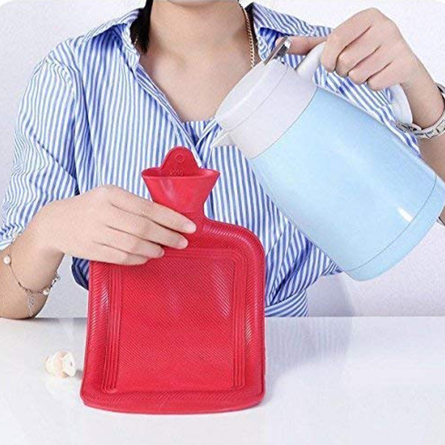Person filling a red rubber hot water bag for pain relief with water from a blue kettle