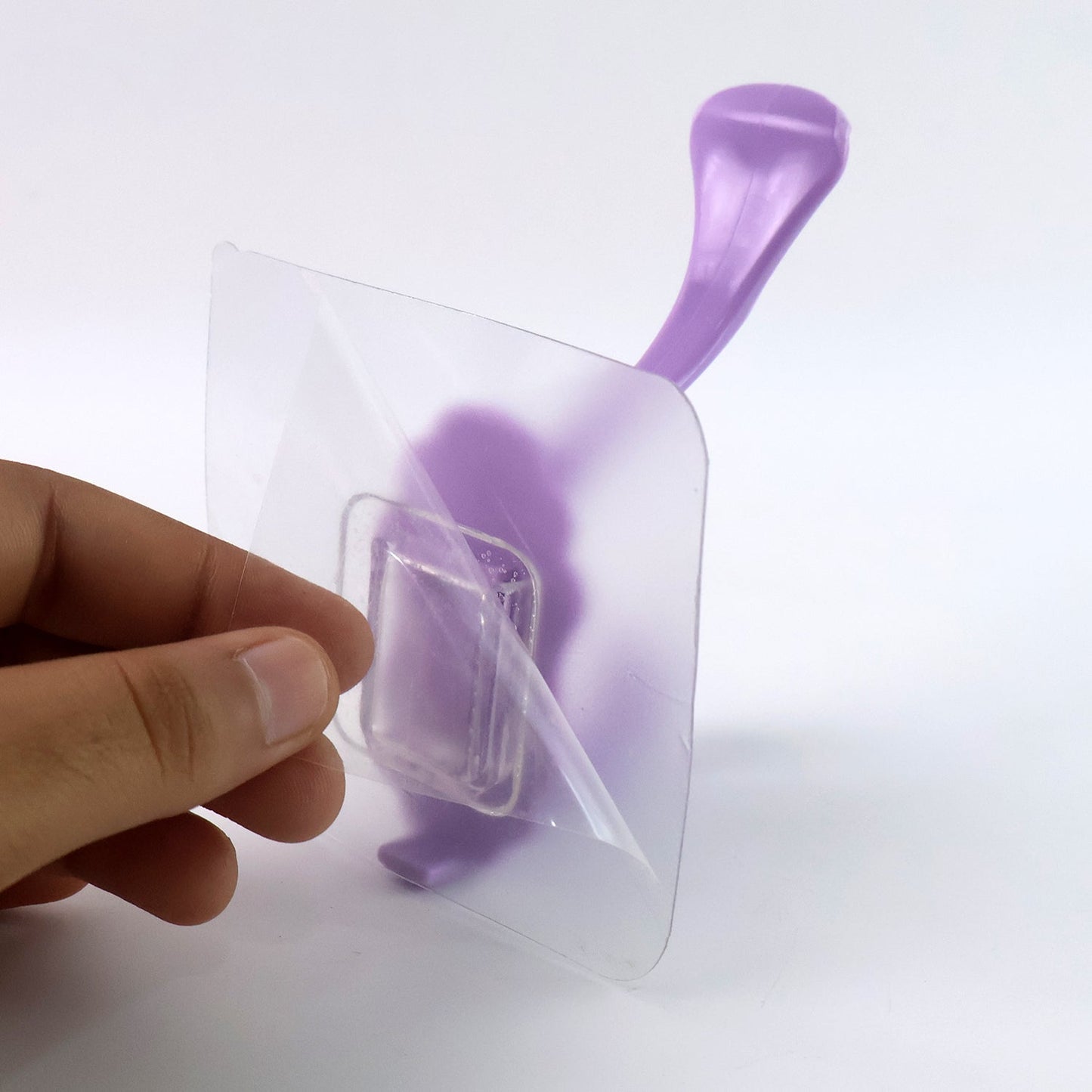 Self-adhesive heavy duty wall hook being peeled from packaging for easy installation