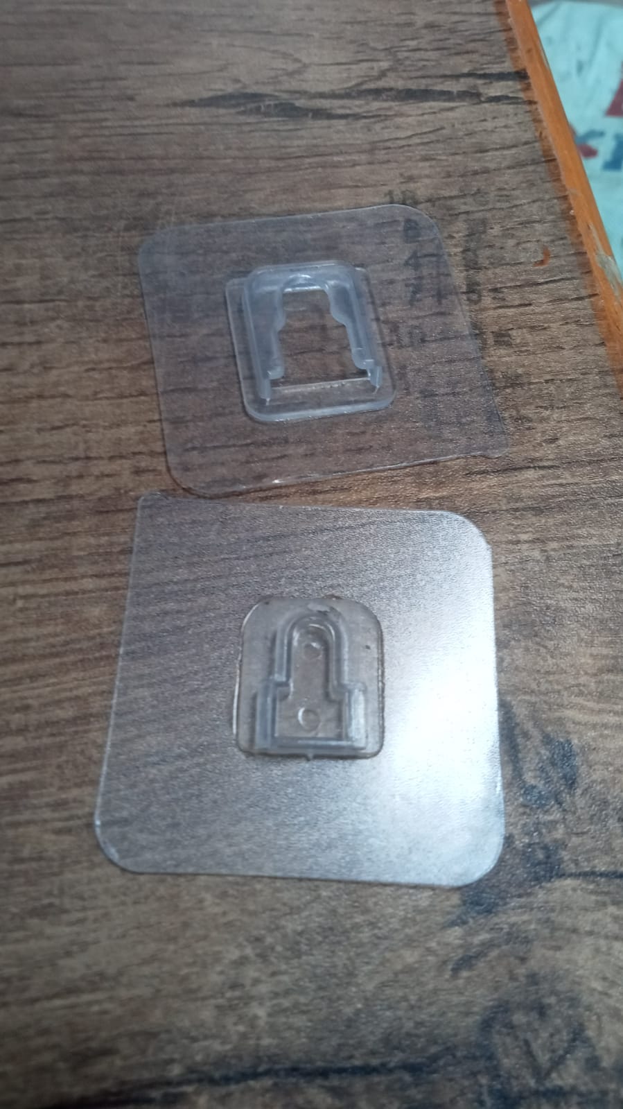 Two self adhesive transparent wall hooks on a wooden surface designed for easy installation