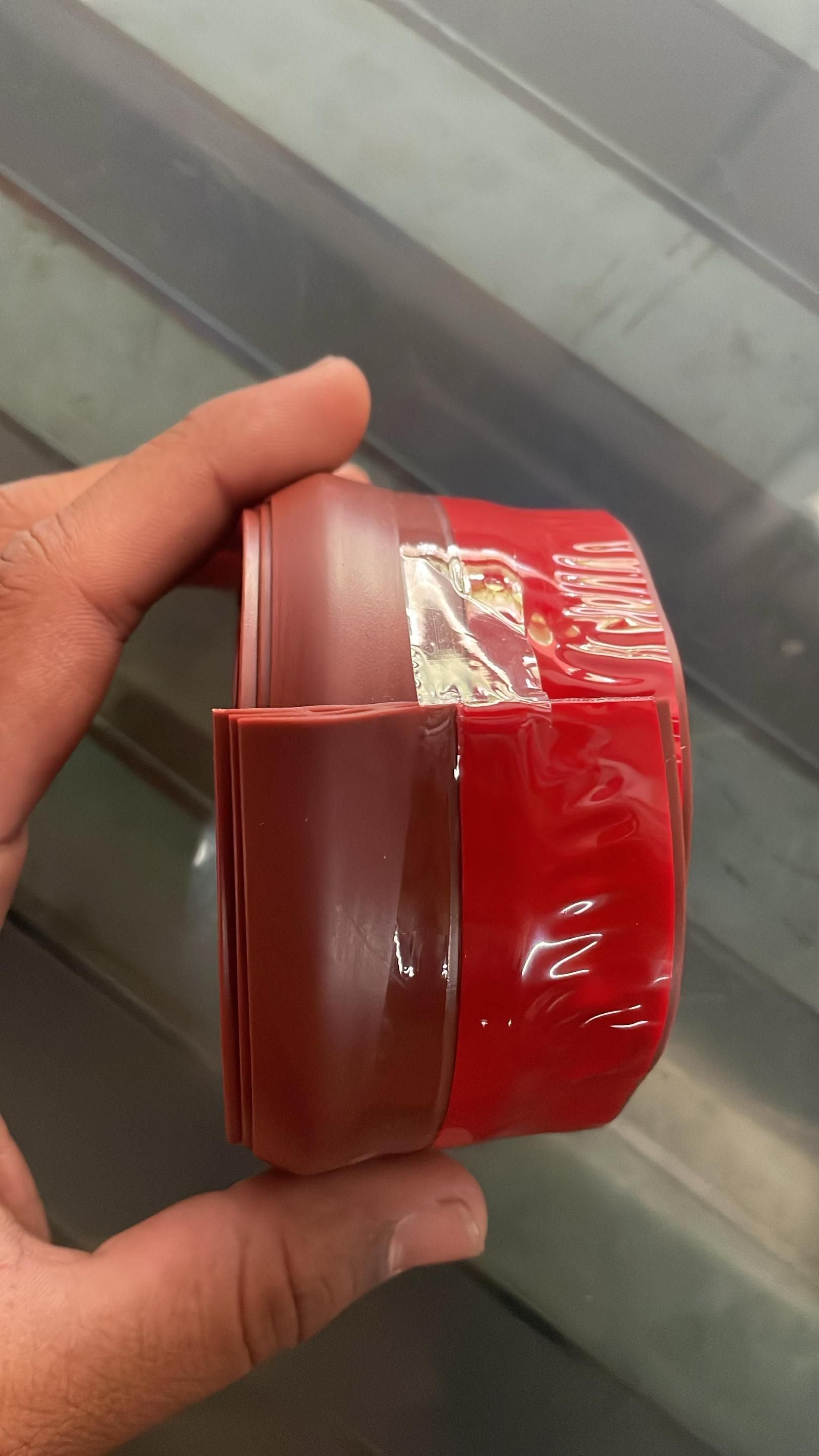 Roll of brown self-adhesive wood floor transition strip held in hand against a tile background