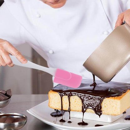 Chef using a silicone baking spatula to drizzle chocolate on a sponge cake in a modern kitchen