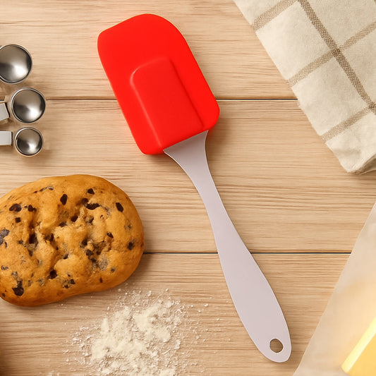 Red silicone baking spatula on a wooden table with cookie dough and measuring spoons