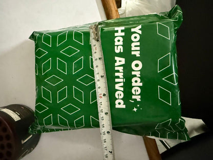 Green package labeled 'Your Order Has Arrived' with measuring tape and a dark object beside it