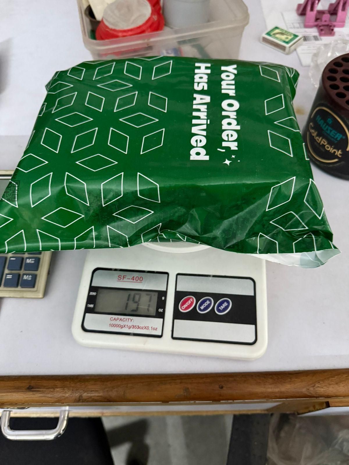 Green packaging labeled Your Order Has Arrived on a scale, ready for shipping of stainless steel pet grooming glove