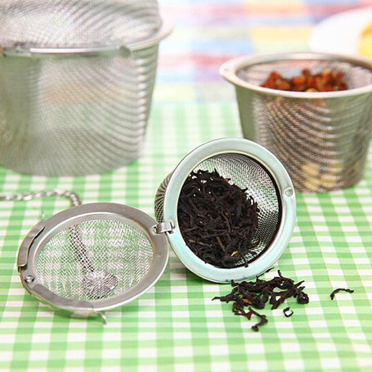 Your Brand stainless steel tea filter with loose tea inside on a green checkered tablecloth