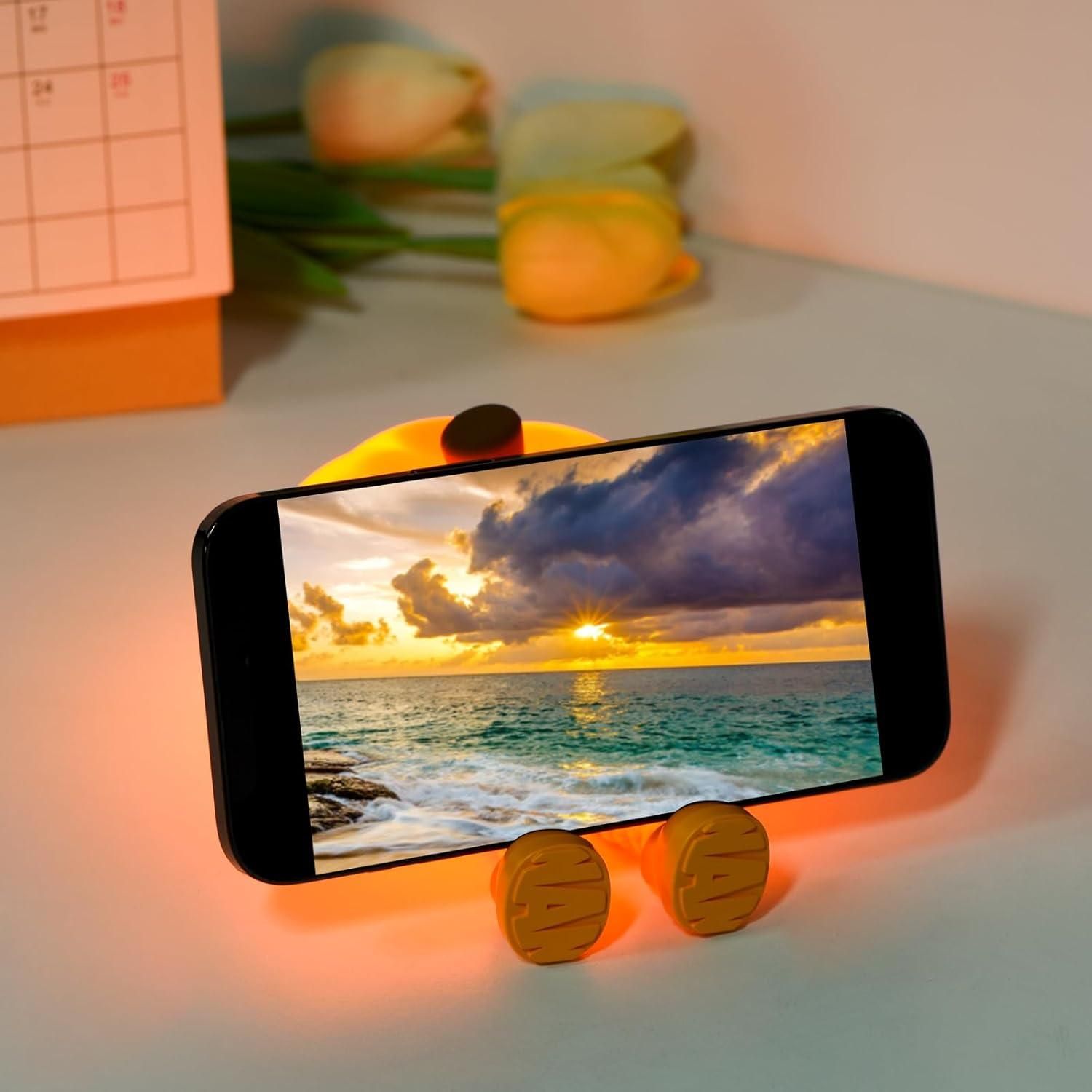 THE GIR FARMER touch control silicone lamp glowing orange holding smartphone on desk with flowers