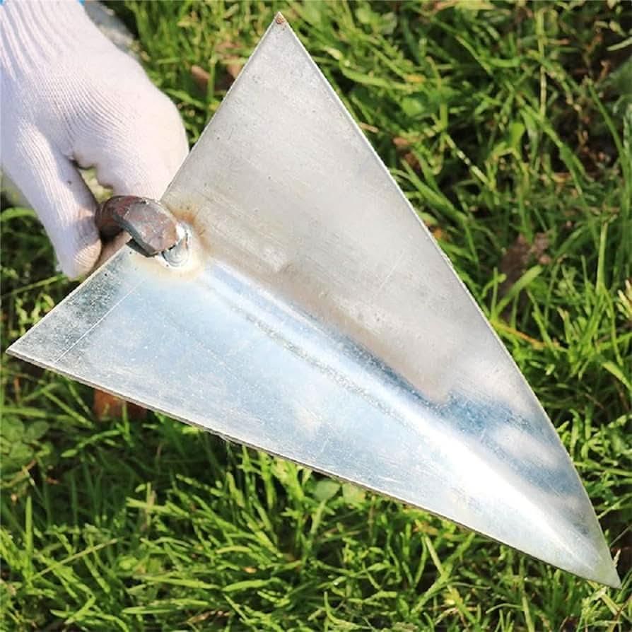 Hand holding a triangle weed remover tool with metal blade over green grass background