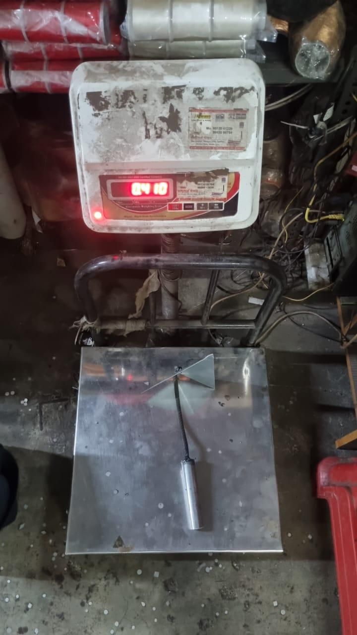 Triangle weed remover tool with metal handle placed on a weighing scale in a workshop