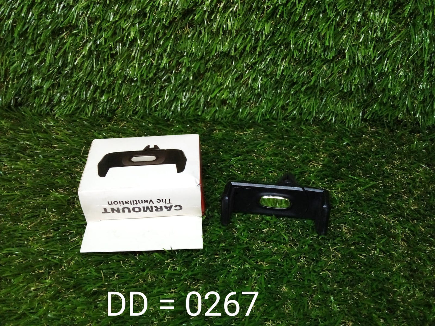 Universal car air vent phone holder in black with packaging displayed on grass background