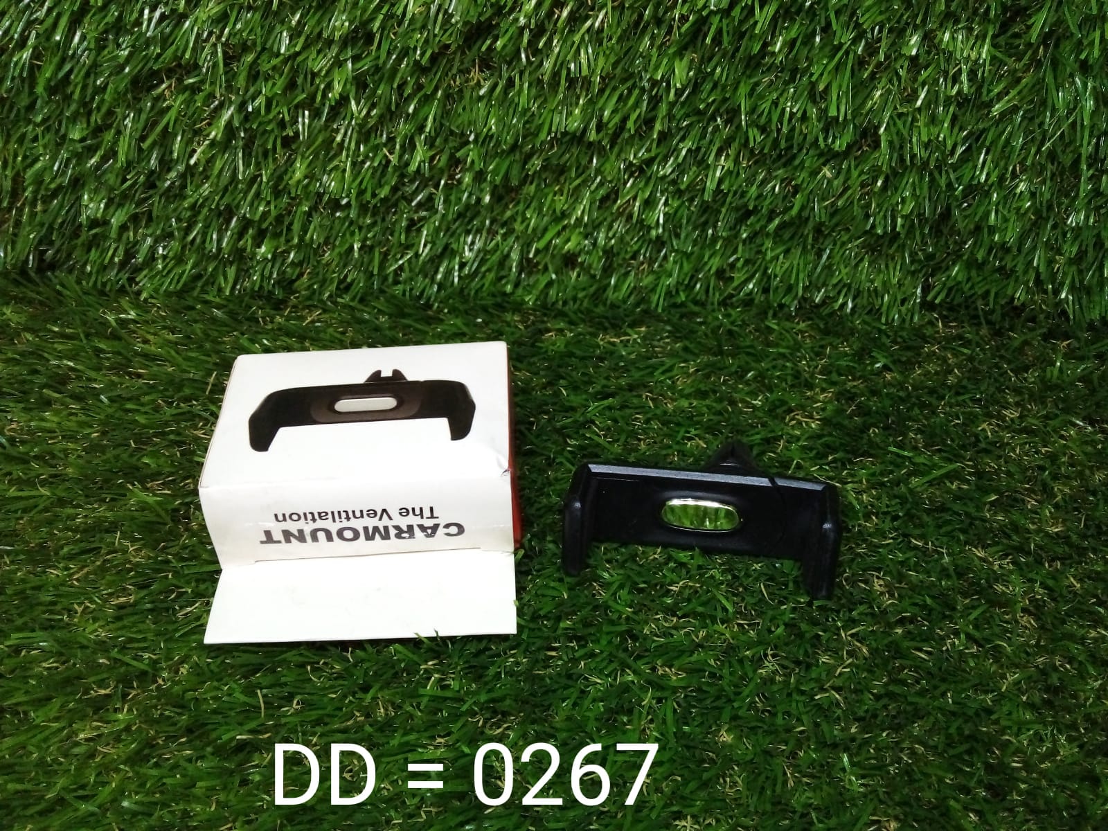 Universal car air vent phone holder in black with packaging displayed on grass background