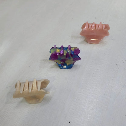 Set of three small hair claw clips for women in pink, beige, and multicolor on white surface