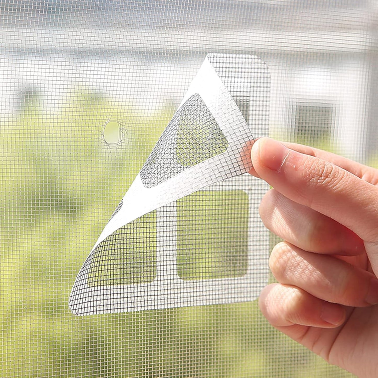 Flexible window screen repair tape being applied to fix a mesh screen tear